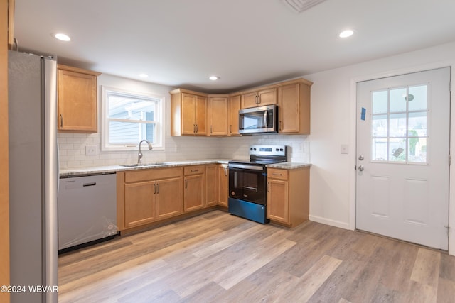 kitchen with light stone countertops, backsplash, stainless steel appliances, sink, and light hardwood / wood-style flooring