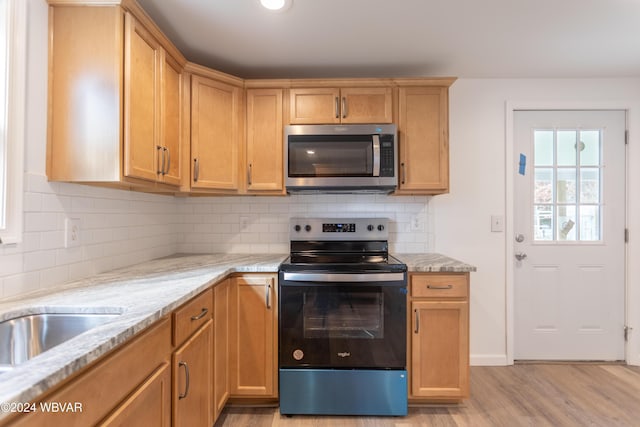 kitchen featuring backsplash, light stone counters, stainless steel appliances, and light hardwood / wood-style flooring