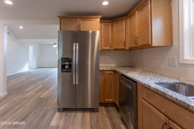 kitchen featuring decorative backsplash, appliances with stainless steel finishes, light stone counters, ceiling fan, and light hardwood / wood-style floors