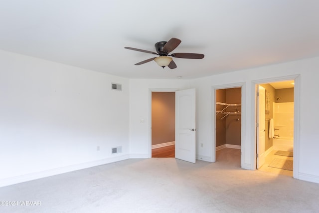 unfurnished bedroom featuring ceiling fan, connected bathroom, a spacious closet, light colored carpet, and a closet