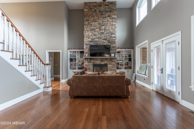 living room featuring french doors, a stone fireplace, dark hardwood / wood-style floors, and a high ceiling