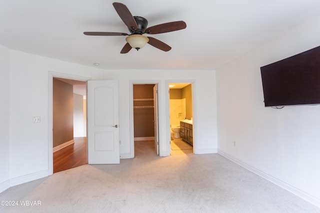 unfurnished bedroom featuring connected bathroom, a walk in closet, ceiling fan, light carpet, and a closet