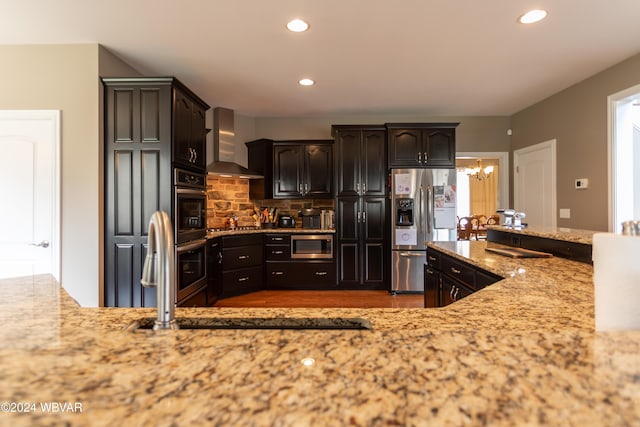 kitchen featuring appliances with stainless steel finishes, sink, backsplash, light stone counters, and wall chimney exhaust hood