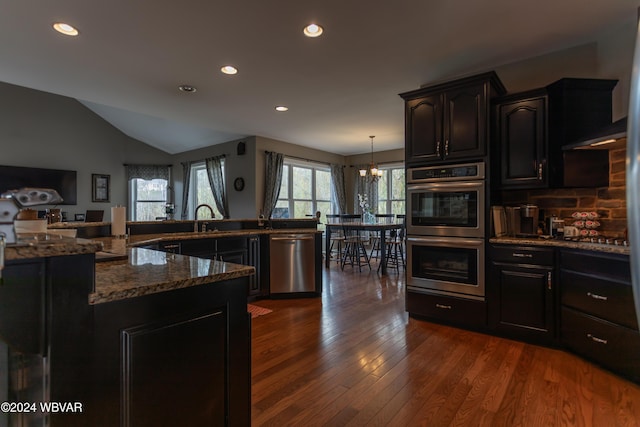 kitchen with lofted ceiling, dark stone countertops, dark hardwood / wood-style flooring, hanging light fixtures, and stainless steel appliances