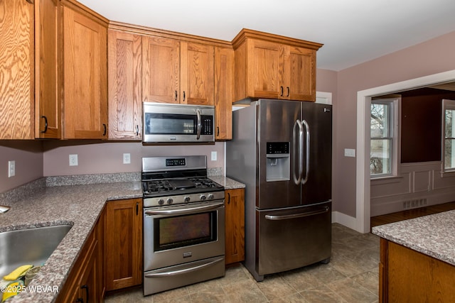 kitchen featuring brown cabinets, stainless steel appliances, visible vents, a sink, and light stone countertops