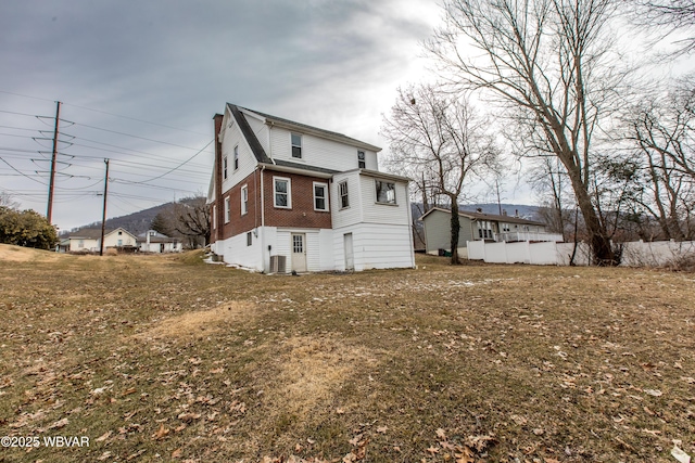 back of property featuring central AC unit, a lawn, and brick siding