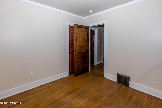 empty room featuring baseboards, crown molding, visible vents, and wood finished floors