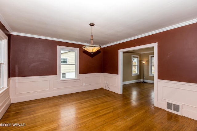 spare room featuring a wainscoted wall, visible vents, wood finished floors, and ornamental molding