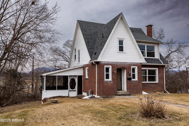 view of front of house with a sunroom, a shingled roof, a front yard, and brick siding