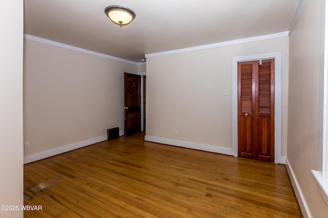 empty room with light wood-type flooring, baseboards, and crown molding