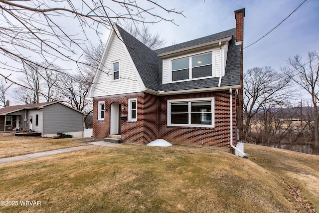 view of front facade with entry steps, brick siding, a shingled roof, a front lawn, and a chimney