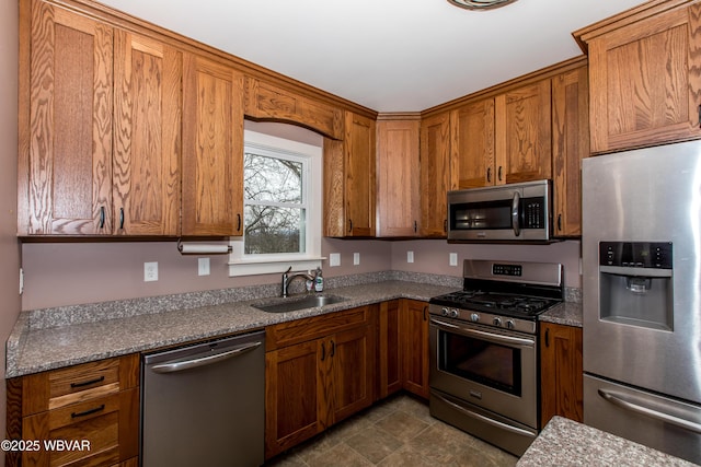 kitchen featuring appliances with stainless steel finishes, brown cabinetry, a sink, and light stone counters