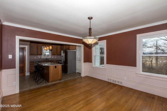 kitchen featuring a breakfast bar, a kitchen island, visible vents, freestanding refrigerator, and pendant lighting