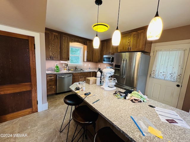 kitchen featuring appliances with stainless steel finishes, light stone counters, pendant lighting, and sink