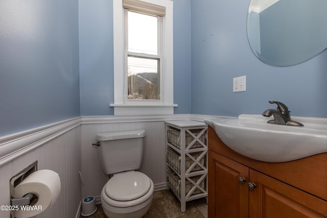 half bath with a wainscoted wall, toilet, and vanity