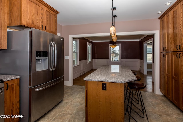 kitchen featuring brown cabinets, a kitchen island, light stone countertops, stainless steel fridge, and a kitchen bar