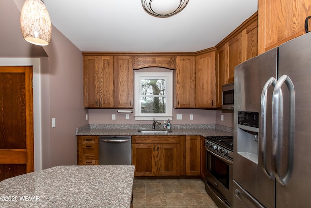 kitchen with light stone counters, a sink, hanging light fixtures, appliances with stainless steel finishes, and brown cabinetry