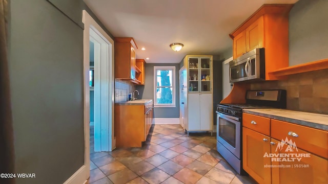 kitchen with decorative backsplash, appliances with stainless steel finishes, light tile patterned flooring, and sink