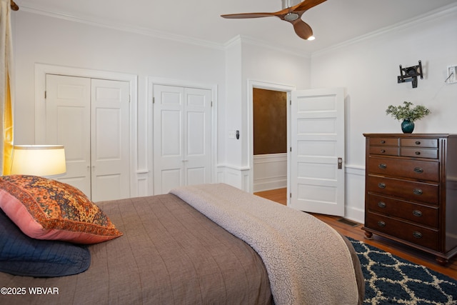bedroom featuring crown molding, ceiling fan, dark wood finished floors, and multiple closets