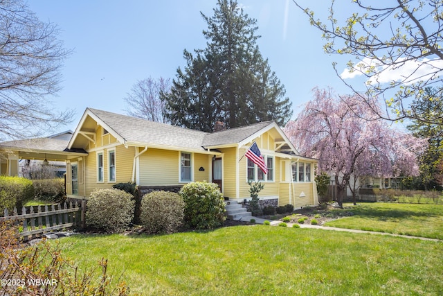 view of front facade featuring roof with shingles, a chimney, a front yard, and fence