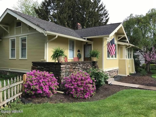 view of front of house featuring fence, stone siding, and a shingled roof
