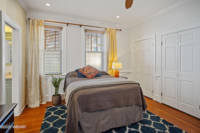 bedroom with crown molding, wood finished floors, two closets, and recessed lighting