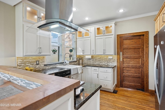 kitchen with island exhaust hood, white cabinetry, backsplash, stainless steel appliances, and light wood finished floors