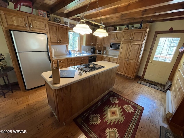 kitchen with appliances with stainless steel finishes, light wood-style flooring, light countertops, beamed ceiling, and a sink