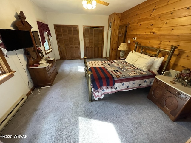 bedroom featuring a baseboard radiator, carpet, wooden walls, multiple closets, and ceiling fan