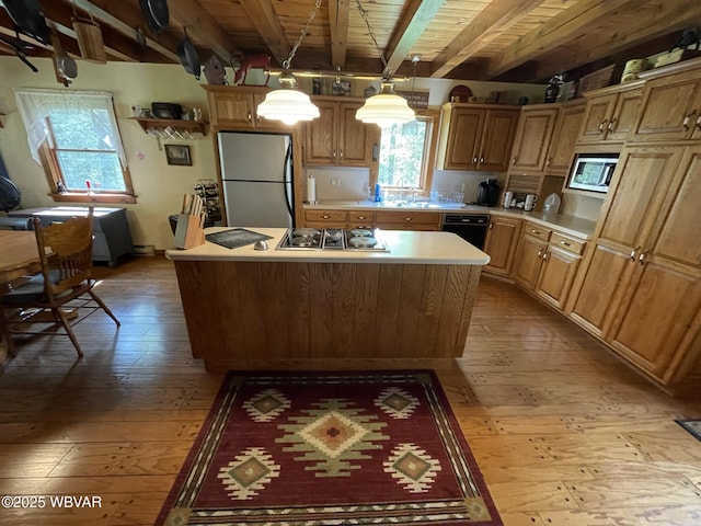 kitchen featuring freestanding refrigerator, light wood-style floors, beamed ceiling, stainless steel microwave, and a kitchen island