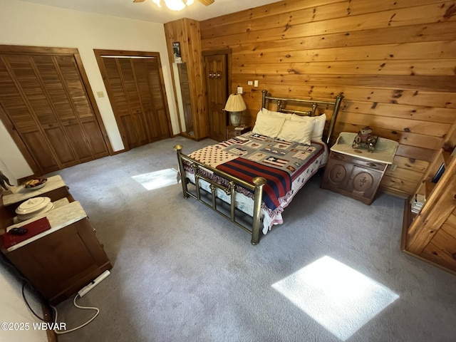 carpeted bedroom featuring two closets and wooden walls