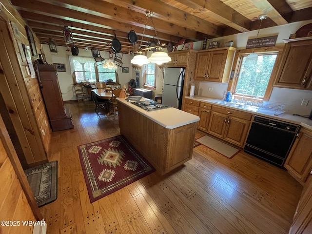 kitchen featuring stainless steel appliances, a sink, light wood finished floors, light countertops, and a center island