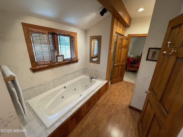 bathroom with wood finished floors, vaulted ceiling, a tub with jets, and ensuite bath