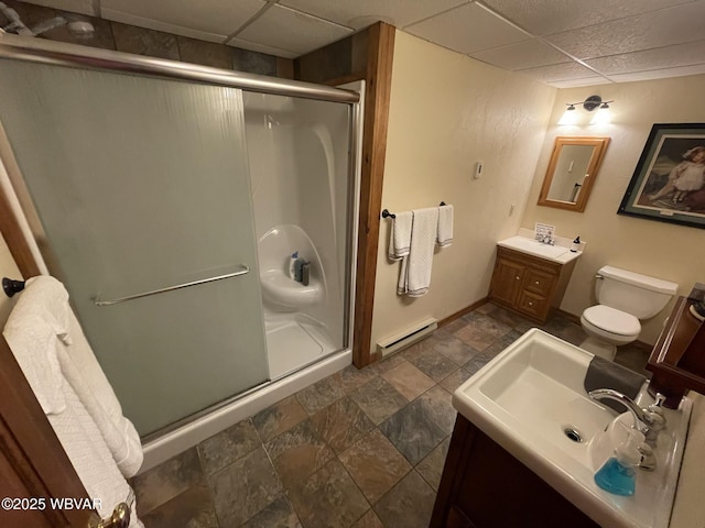 full bathroom with a stall shower, a baseboard heating unit, stone finish flooring, vanity, and a paneled ceiling
