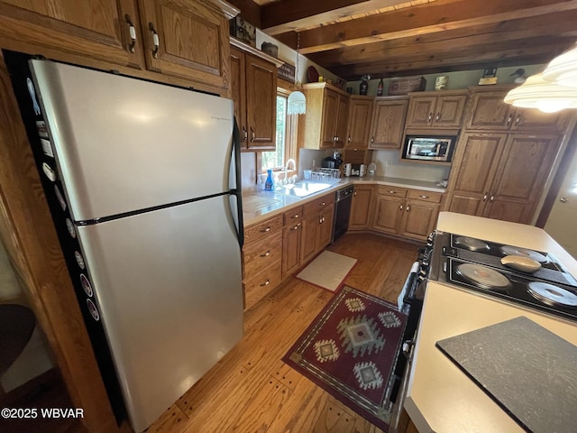 kitchen with stainless steel appliances, a sink, light wood finished floors, light countertops, and beam ceiling
