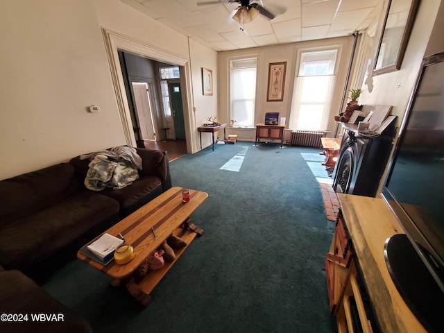 carpeted living room with ceiling fan and radiator