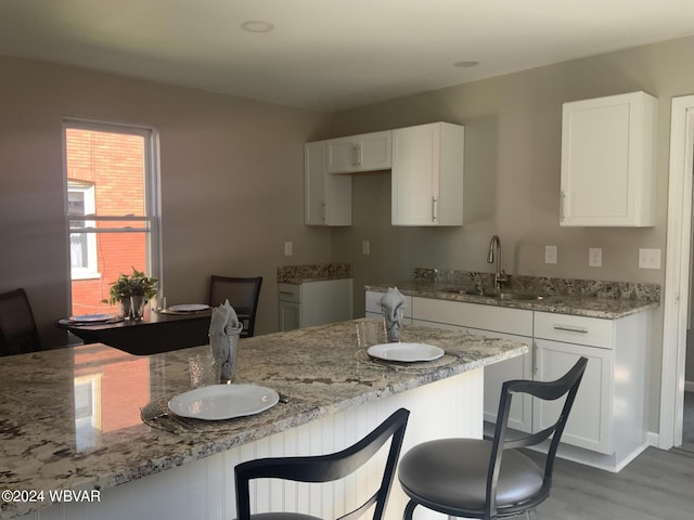 kitchen with light stone countertops, sink, white cabinets, and light hardwood / wood-style floors