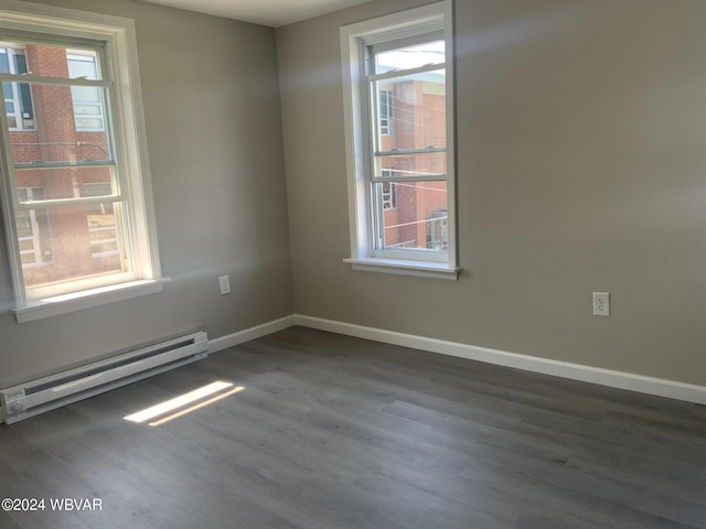 empty room featuring a healthy amount of sunlight, dark hardwood / wood-style flooring, and a baseboard heating unit