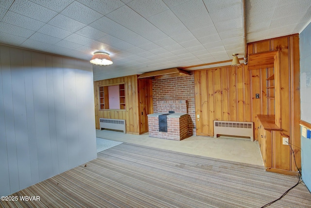 interior space featuring carpet flooring, radiator, a brick fireplace, and wood walls
