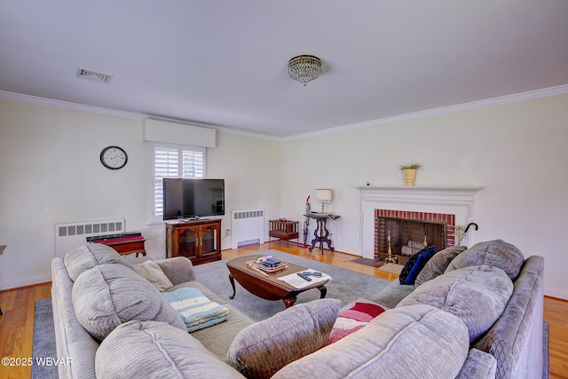 living room featuring visible vents, crown molding, a brick fireplace, wood finished floors, and radiator