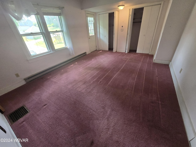 unfurnished bedroom with baseboard heating, dark colored carpet, and two closets