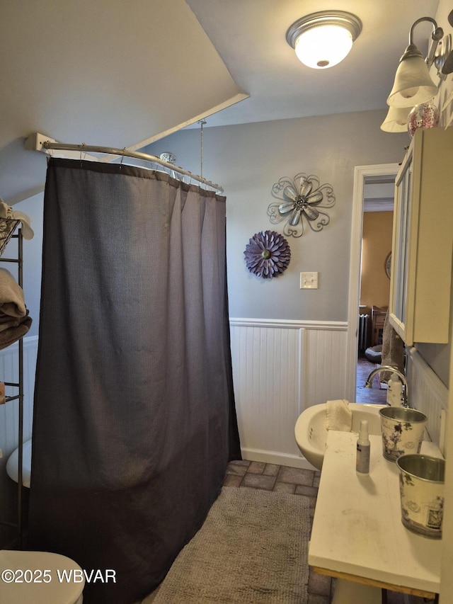 full bath featuring toilet, a wainscoted wall, curtained shower, and a sink