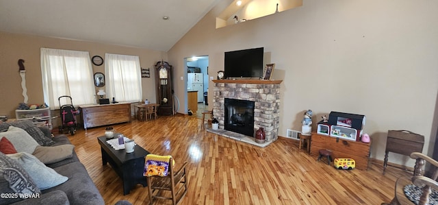 living room with wood-type flooring, a stone fireplace, and high vaulted ceiling