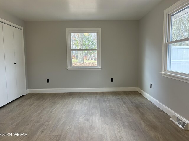 unfurnished bedroom with a closet, light hardwood / wood-style floors, and multiple windows