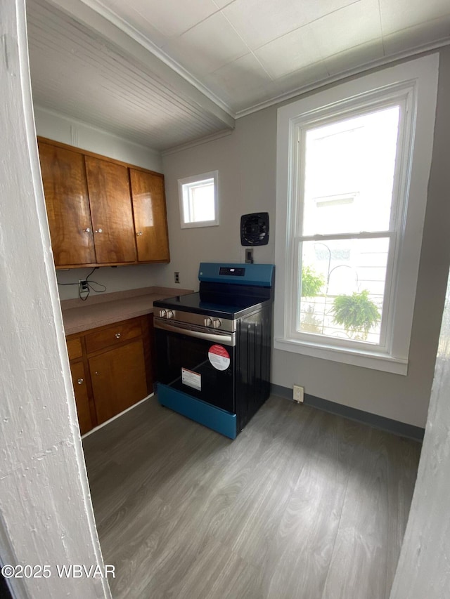 kitchen with brown cabinetry, crown molding, wood finished floors, stainless steel range with electric stovetop, and baseboards
