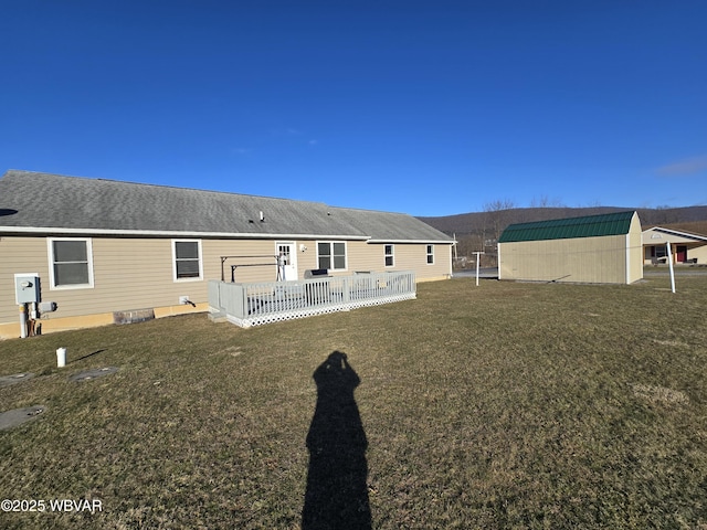 back of house with a deck, an outbuilding, and a lawn