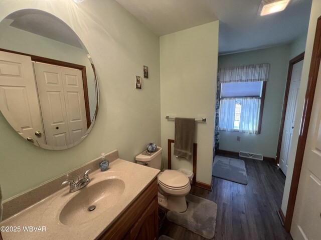 bathroom featuring visible vents, baseboards, toilet, wood finished floors, and vanity