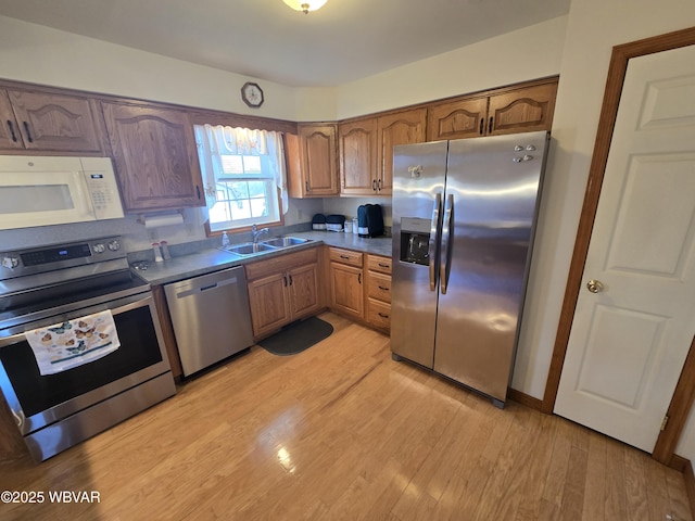 kitchen with brown cabinetry, light wood-style flooring, a sink, appliances with stainless steel finishes, and dark countertops