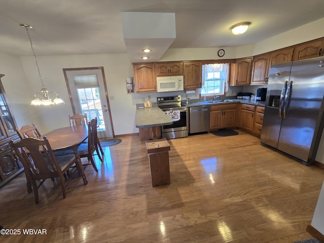 kitchen featuring wood finished floors, a peninsula, a sink, appliances with stainless steel finishes, and a chandelier