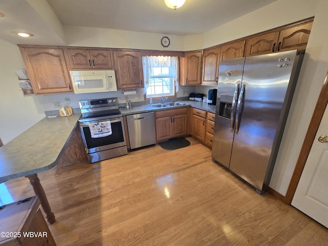 kitchen with light wood-type flooring, a sink, appliances with stainless steel finishes, a peninsula, and brown cabinetry